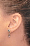 A close-up of a woman's ear wearing a silver-toned dangle earring with a clear round crystal and a dangling clear quartz crystal.

